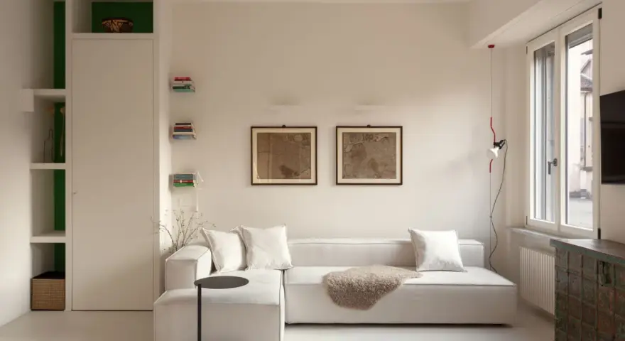 Soggiorno luminoso con divano bianco, quadri antichi e arredi funzionali, perfetto per case piccole ben arredate.