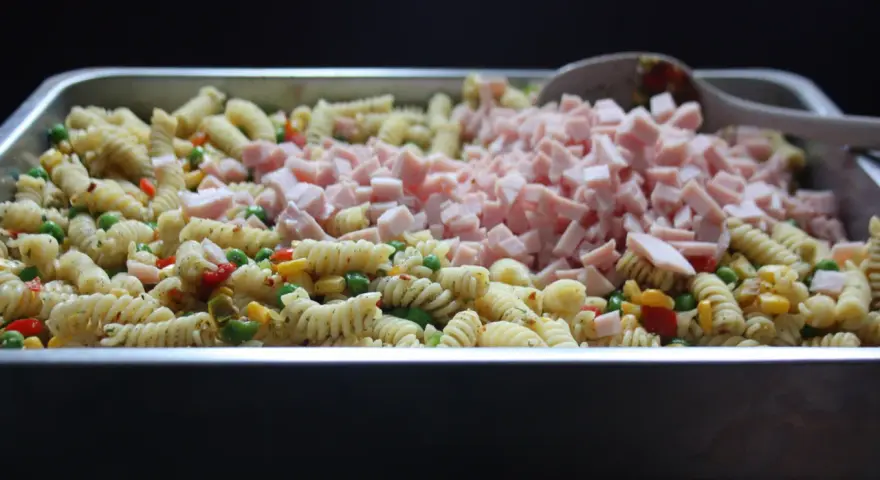 Stor ugnsform fylld med pastasallad med kassler, grönsaker och en sked.