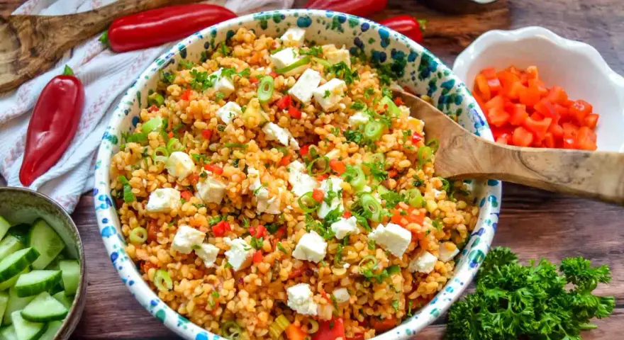Frischer bulgursalat mit feta, Tomaten, Paprika und Frühlingszwiebeln, garniert mit Petersilie.