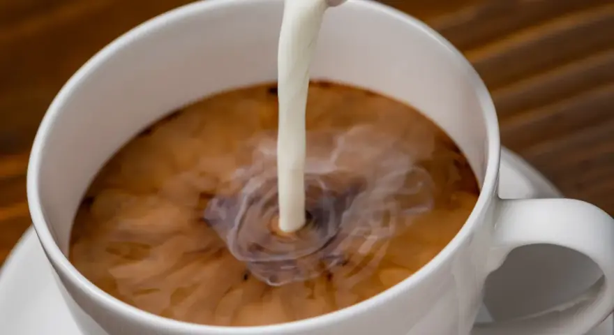 Biała filiżanka kawy, do której wlewane jest mleko. Zastanawiasz się nad mleko owsiane kcal?