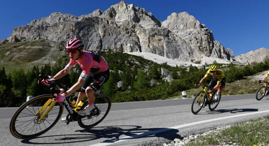 Cyclist in pink jersey, likely the winner of the Giro d'Italia, climbs a mountain road with a dramatic rocky peak behind.