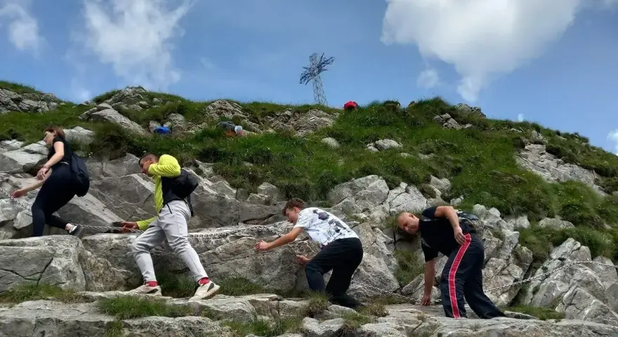 Grupa turystów wspina się po kamienistym zboczu, pokonując najtrudniejszy szlak na Giewont. W tle widoczny krzyż.
