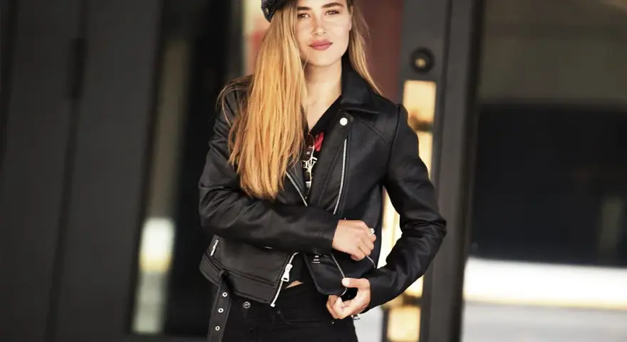 Dziewczyna w czarnej ramonesce i czapce, emanująca pewnością siebie w stylu glam rock.