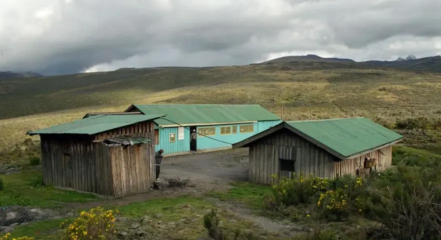 Proste chatki z zielonymi dachami na tle surowego krajobrazu u podnóża góry Mt Kenya.