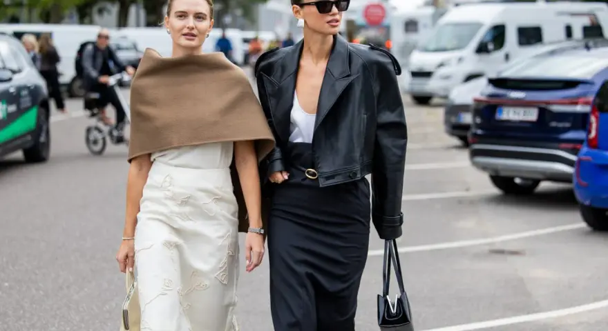 Dwie kobiety prezentują, co jest teraz modne: elegancka czarna ramoneska i kremowa spódnica z subtelnymi zdobieniami.