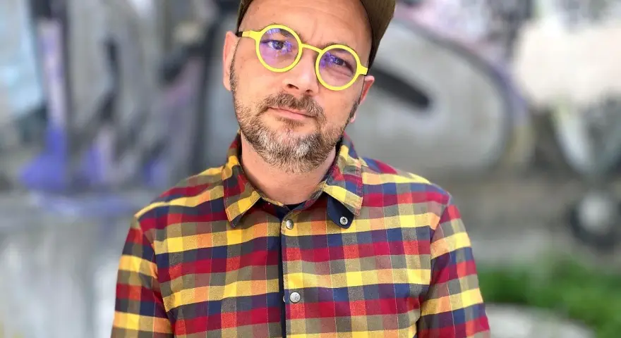 Filip Springer w okularach i koszuli w kratę, na tle graffiti.