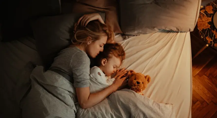 Mutter und Kind schlafen eng umschlungen. Ab wann Babys bewusst kuscheln, zeigt diese Szene der Geborgenheit.