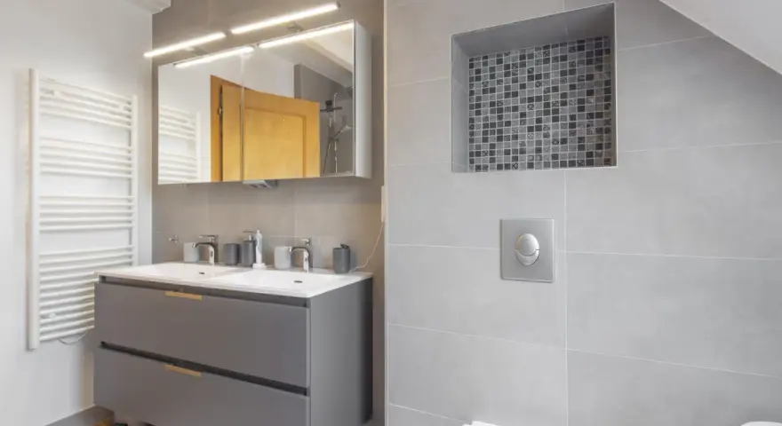 Salle de bain moderne avec double vasque, radiateur blanc et un choix carrelage gris subtil, agrémenté d'une niche décorative en mosaïque.