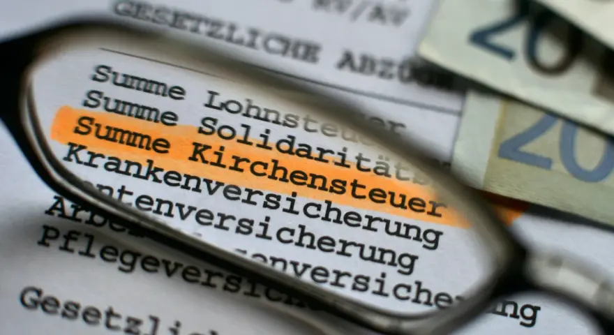 Durch eine Lupe wird die "Summe Kirchensteuer" auf einem Dokument hervorgehoben. Dies zeigt, wo Kirchensteuer anfällt.