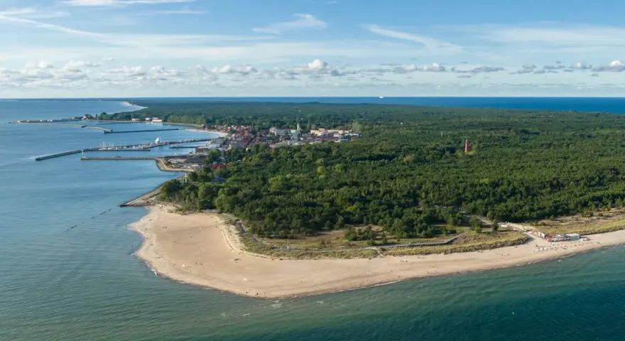 Widok na zatokę pucką z lotu ptaka. Widać piaszczystą plażę, las sosnowy, miasteczko z portem i latarnię morską.