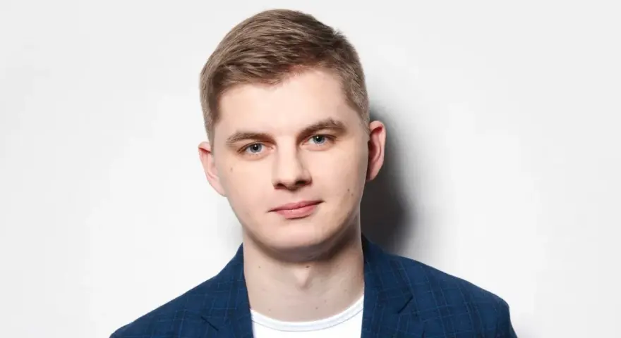 Młody mężczyzna w niebieskiej marynarce w kratę, gotowy do występu. Polski stand up w jego wykonaniu to gwarancja dobrej zabawy.