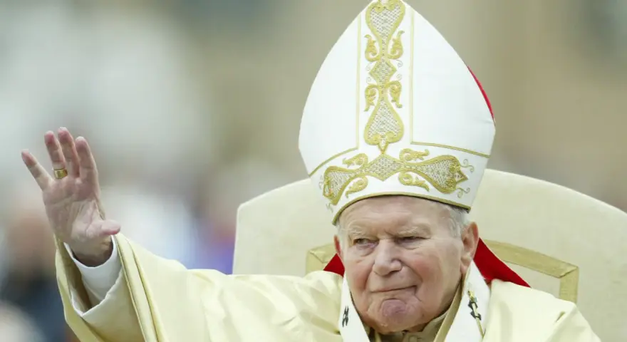 Papież Jan Paweł II w białej mitrze z haftem, pozdrawia wiernych. Jego dłoń z pierścieniem jest uniesiona. Codzienna modlitwa do św. Jana Pawła II.