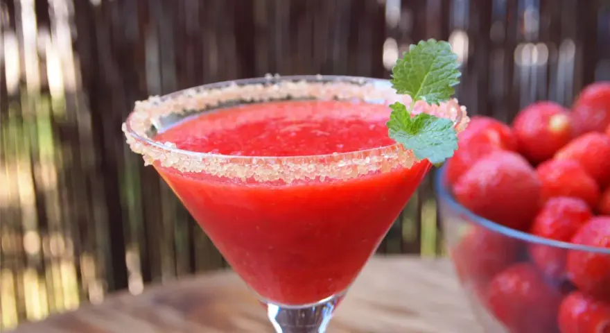 Orzeźwiający strawberry daiquiri z cukrowym rantem i listkiem mięty, obok miska pełna świeżych truskawek.