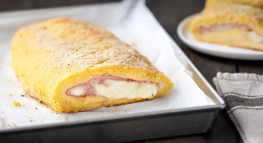 Rotolo dorato di polpettone di patate ripieno di prosciutto e formaggio filante, pronto per essere gustato.