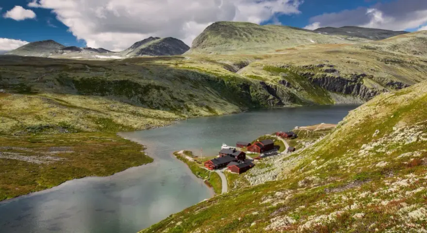 En vacker vy över en sjö med röda stugor vid en fjällsluttning, perfekt för en triangeltur i Norge.