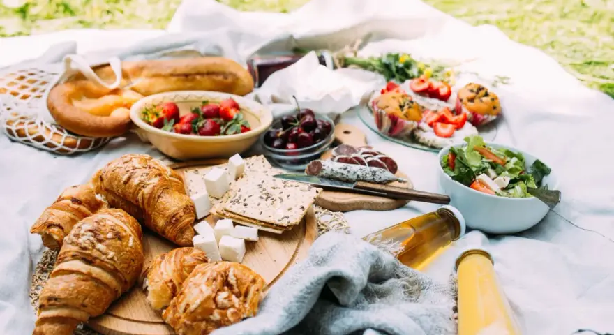 Pyszne jedzenie na piknik: świeże pieczywo, owoce, sałatka, sery i napoje.