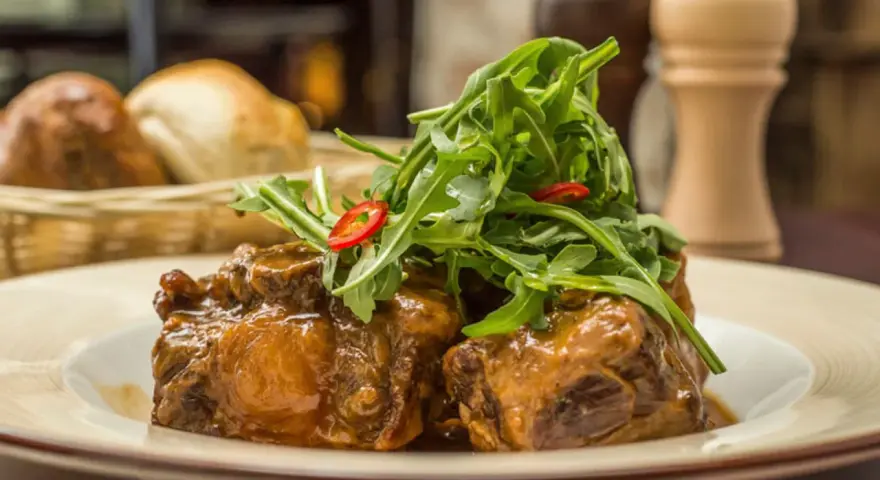 Delicioso rabo de toro en salsa, coronado con rúcula fresca y rodajas de chile. Una receta que conquista paladares.