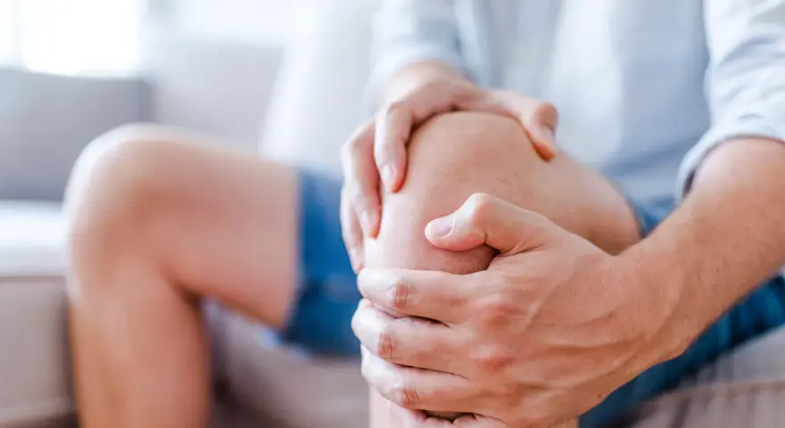 Mężczyzna trzyma się za kolano, odczuwając rwący ból kolana w spoczynku.