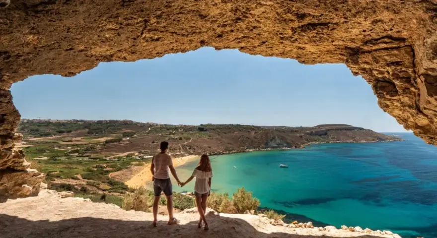 Para w jaskini podziwia widok na turkusowe morze i plażę. Malta pogoda wrzesień idealna na wakacje.