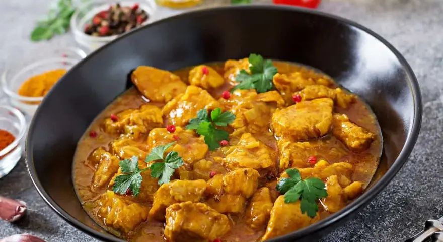 Aksamitny kurczak w sosie curry, jedno z popularnych potraw kuchni azjatyckiej, ozdobiony natką pietruszki i różowym pieprzem.