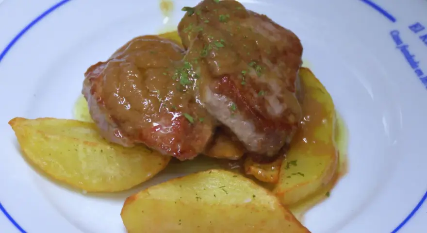Solomillo jugoso con salsa de whisky sobre patatas gajo en un plato blanco.