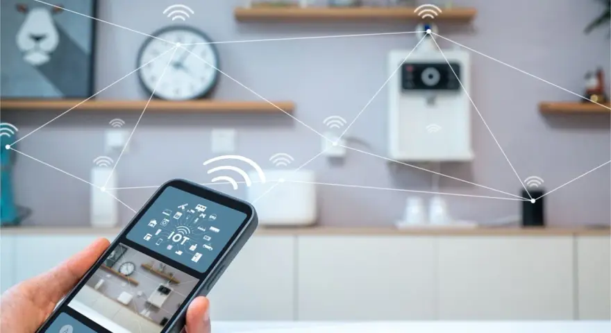 En hand håller en smartphone med en smart life app. I bakgrunden syns ett kök med uppkopplade enheter.