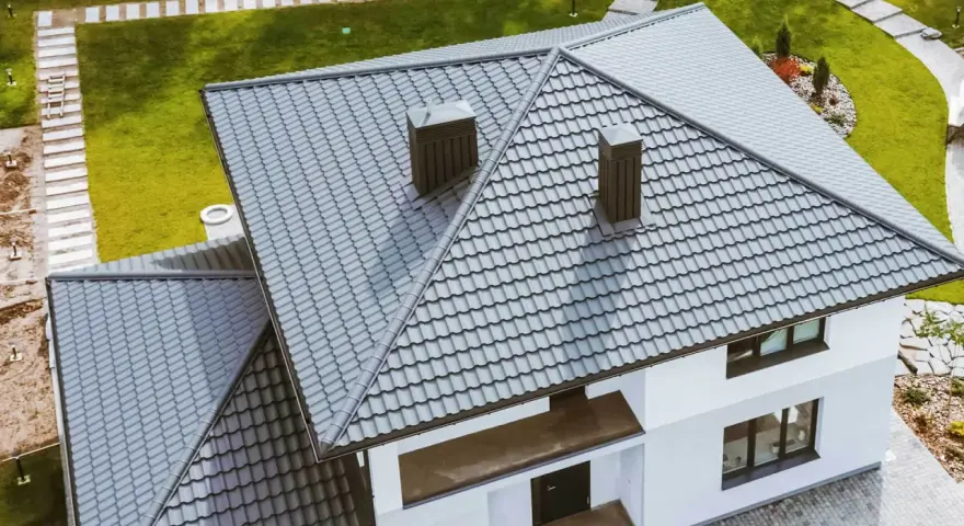 Nowoczesny dom z szarym, czterospadowym dachem z blachodachówki. Dwa kominy wystają ponad linię dachu.