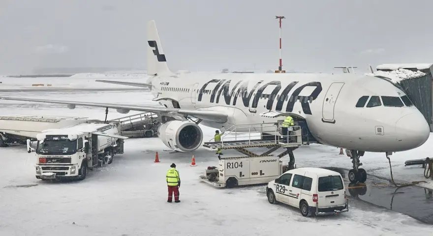 Samolot Finnair na lotnisku w śnieżny dzień. Pracownicy obsługi naziemnej przygotowują samolot do lotu. Czy do Finlandii można lecieć na dowód?
