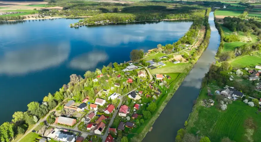 Pławniowice jezioro otoczone zielenią i domkami letniskowymi, z kanałem wodnym biegnącym wzdłuż brzegu.