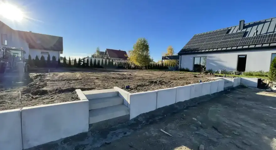 Nowe schody i betonowy murek to co zamiast muru oporowego, otaczają plac budowy domu z panelami słonecznymi.