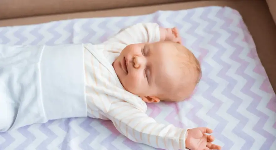 Śpiące niemowlę na kolorowej macie. Średnio główka niemowlaka rośnie ok. 1-2 cm miesięcznie.
