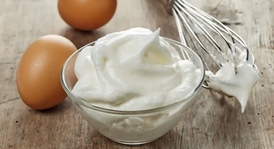 Zwei Eier und ein Schneebesen neben einer Schüssel mit luftigem Eischnee, der nicht fest wird.