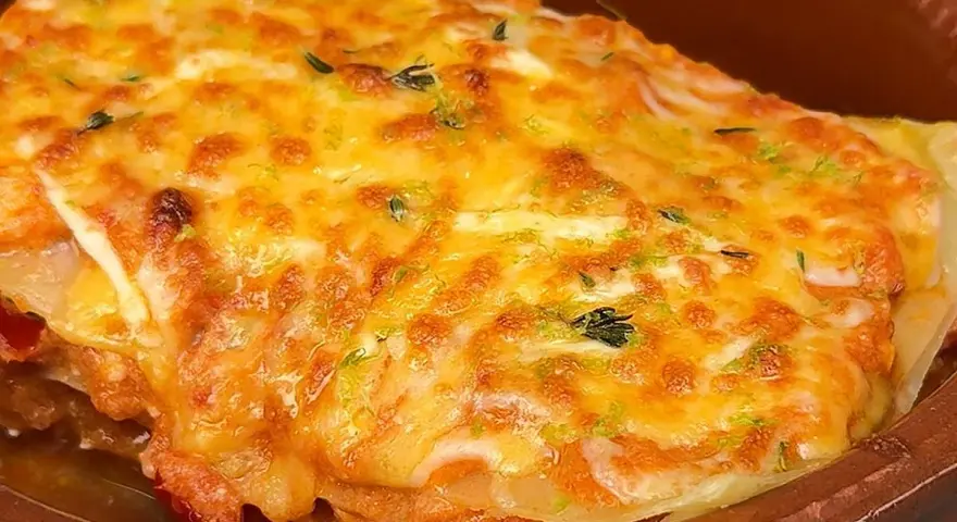 Deliciosa lasaña de atún gratinada con queso dorado y hierbas frescas, servida en una cazuela de barro.