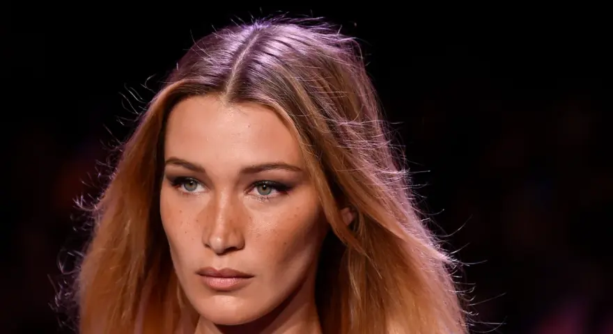 Primo piano di una modella con capelli biondi mossi e occhi verdi penetranti. La sua espressione è enigmatica, quasi a chiedersi chi è la donna più bella del mondo.