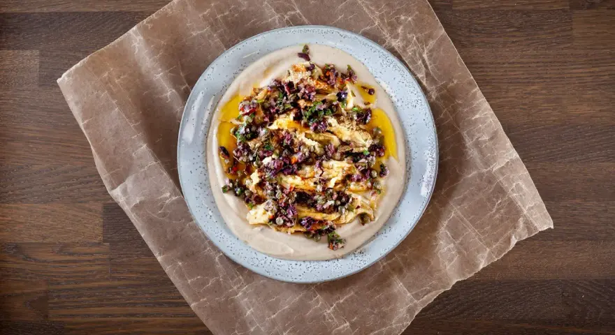 En krämig aubergine i ugn serveras på en bädd av hummus, toppad med en smakrik blandning av oliver, kapris och örter.