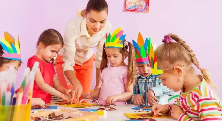 Nauczycielka pomaga dzieciom w tworzeniu pióropuszy. Jedno z dzieci, 4-latek, nie chce się bawić z dziećmi, ale skupia się na pracy.