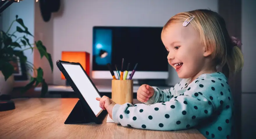 Uśmiechnięta dziewczynka ogląda ulubionych youtuberów dla dzieci na tablecie.