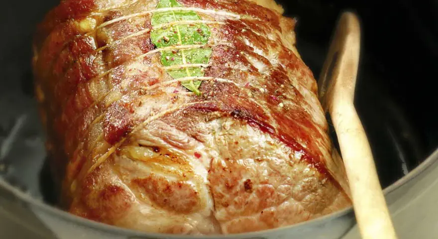 Un rôti de porc cocotte, doré et savoureux, est prêt à cuire dans sa cocotte avec une feuille de laurier et une cuillère en bois.