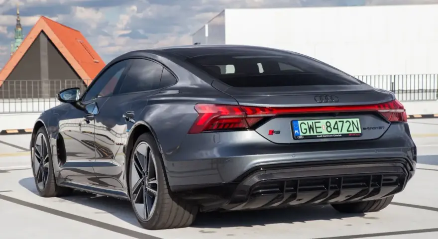 Tył ciemnoszarego Audi RS e-tron GT na parkingu, z widocznymi światłami i tablicą rejestracyjną.