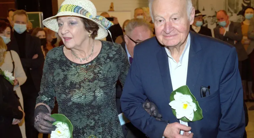Ewa Dałkowska z synem Ksawerym, elegancko ubrani, z kwiatami w dłoniach, podczas uroczystości.