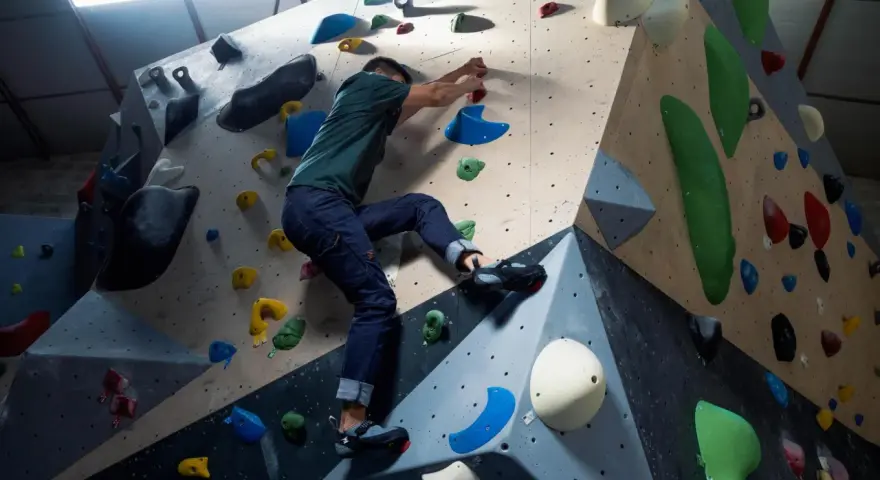 Mann klettert an einer bunten Kletterwand, die aussieht, als ob sie jemand selber bauen könnte.