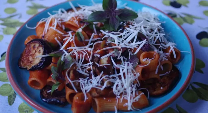 Pyszne danie pasta alla norma z makaronem rigatoni, bakłażanem w sosie pomidorowym i posypane startym serem.