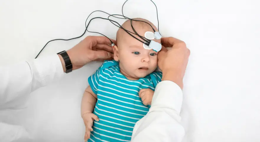 Niemowlę z elektrodami na głowie, przygotowywane do badania słuchu. To ważny krok w diagnostyce, by wcześnie wykryć potrzebę zastosowania aparatu słuchowego dla niemowlaka.