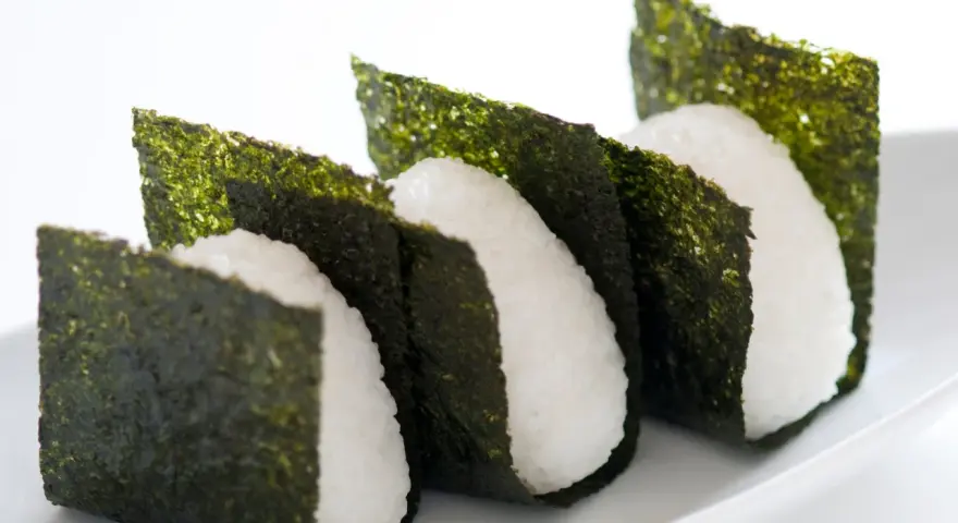 Trzy ryżowe onigiri owinięte w arkusze nori. Prosty sposób, jak przygotować nori do sushi, by nadać mu chrupkość i smak.