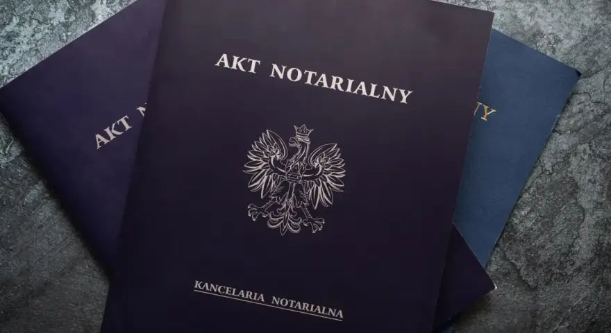 Stos dokumentów, na wierzchu ciemnogranatowy akt notarialny z godłem Polski.