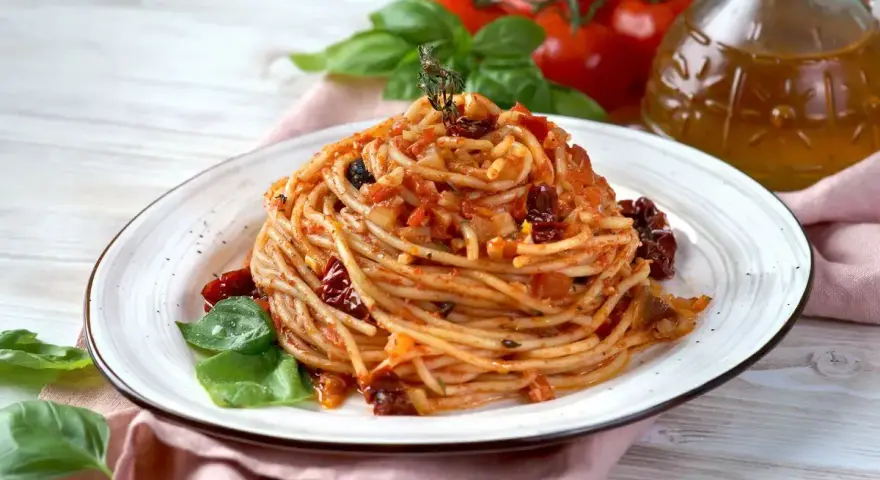 Un piatto di spaghetti conditi con un sugo rosso ricco di pomodori secchi, basilico fresco e un filo d'olio d'oliva.