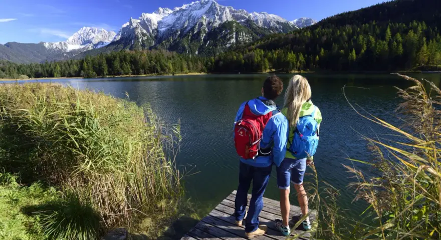 Ein Paar genießt die Aussicht auf die Berge bei Garmisch-Partenkirchen. Sie stehen auf einem Steg am See, bereit zum Wandern.