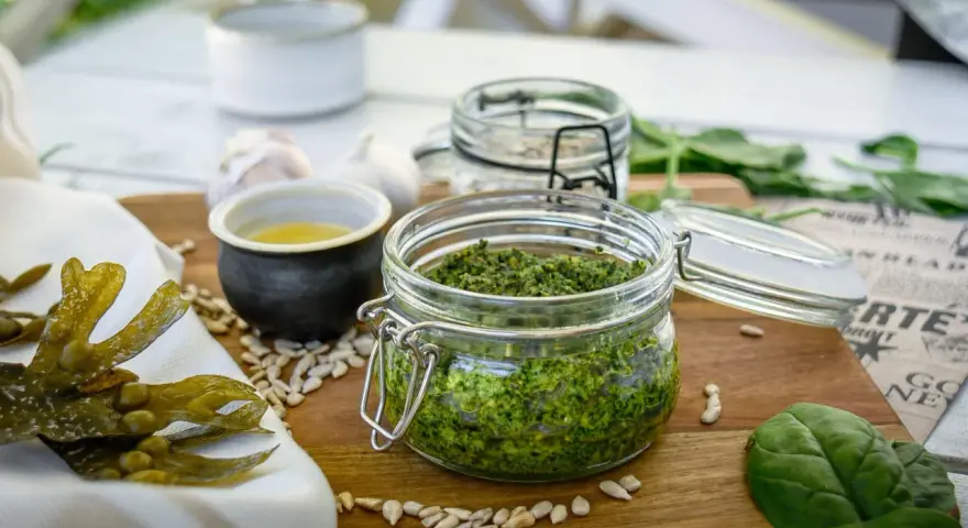 Frisches Pesto aus essbaren Algen der Nordsee, daneben Sonnenblumenkerne, Knoblauch und ein kleines Schälchen mit Öl.