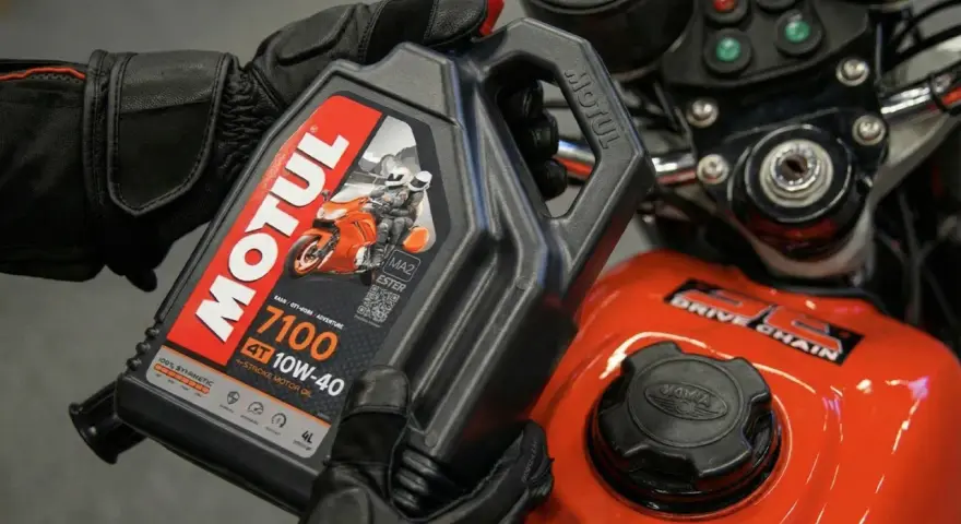 Ręce w rękawiczkach trzymają olej Motul 7100 10W-40. Pytanie: co ile wymieniać olej w motocyklu?