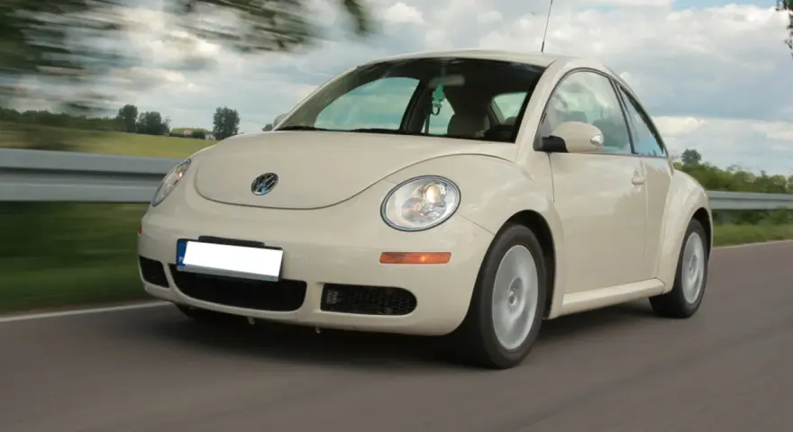 Jasny Volkswagen Beetle w ruchu na drodze, z rozmytym tłem.